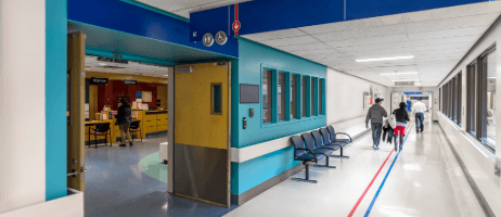 Hospital corridor with teal walls, wood doors, and staff walking down the hall
